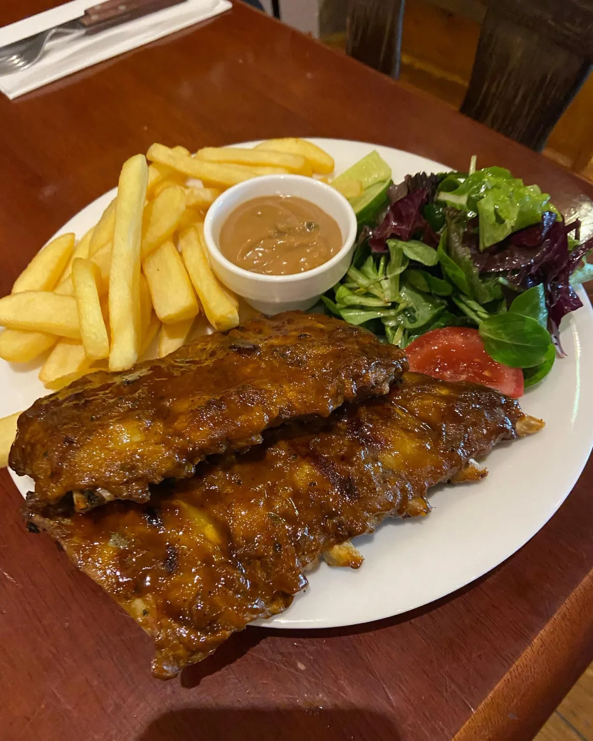 Spareribs from the grill with fries, salad and a pot of sauce on a white plate