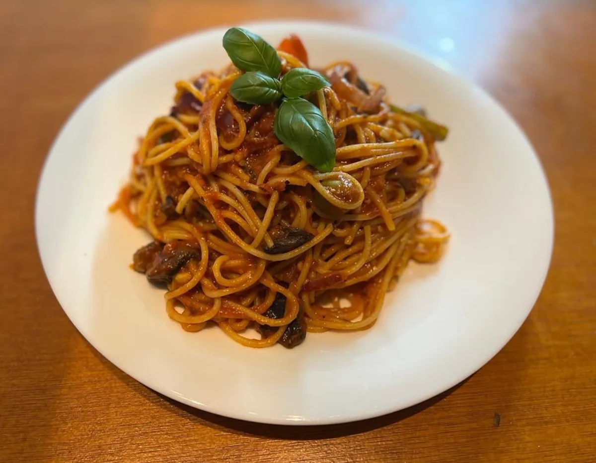 A plate of spaghetti with tomato sauce, olives and fresh basil, on a wooden table